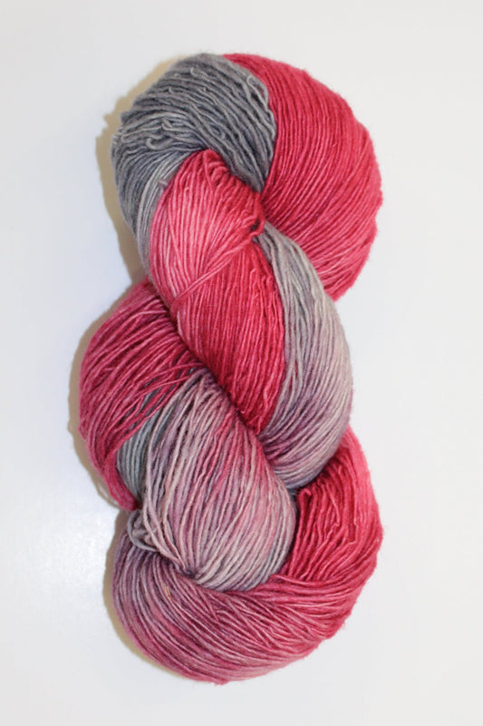 A single skein of variegated yarn in shades of pink, red, and gray, photographed on a plain white background.